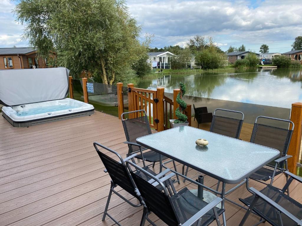 a table and chairs on a deck with a view of a river at Indulgence Lakeside Lodge i2 with hot tub, private fishing peg situated at Tattershall Lakes Country Park in Tattershall