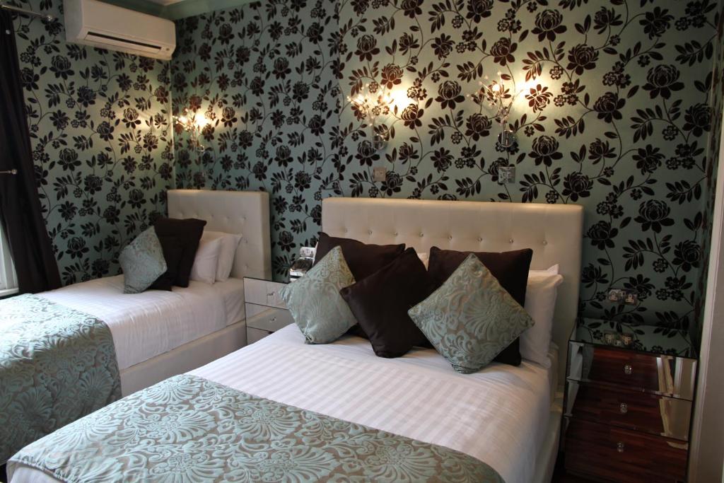 1 dormitorio con 2 camas y papel pintado con motivos florales en Crompton Guest House en Hounslow