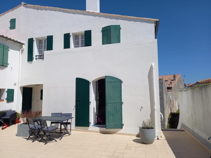 - un bâtiment blanc avec des portes vertes et une table dans l'établissement St Mart. l'îlot Rhéa, à Saint-Martin-de-Ré