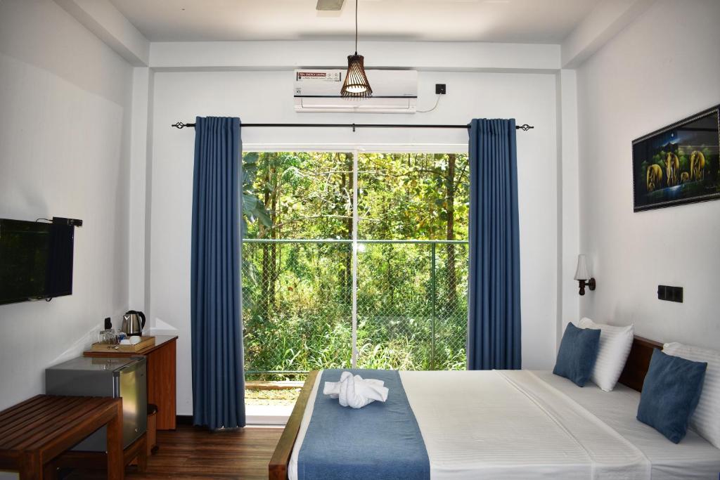 a bedroom with a large window with blue curtains at Forest Edge Safari Villa in Udawalawe