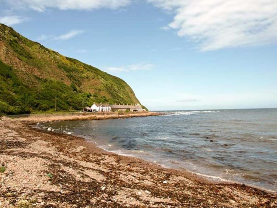 a beach with a house on the side of a hill at The Cottage By The Sea, Scotland in Burnmouth