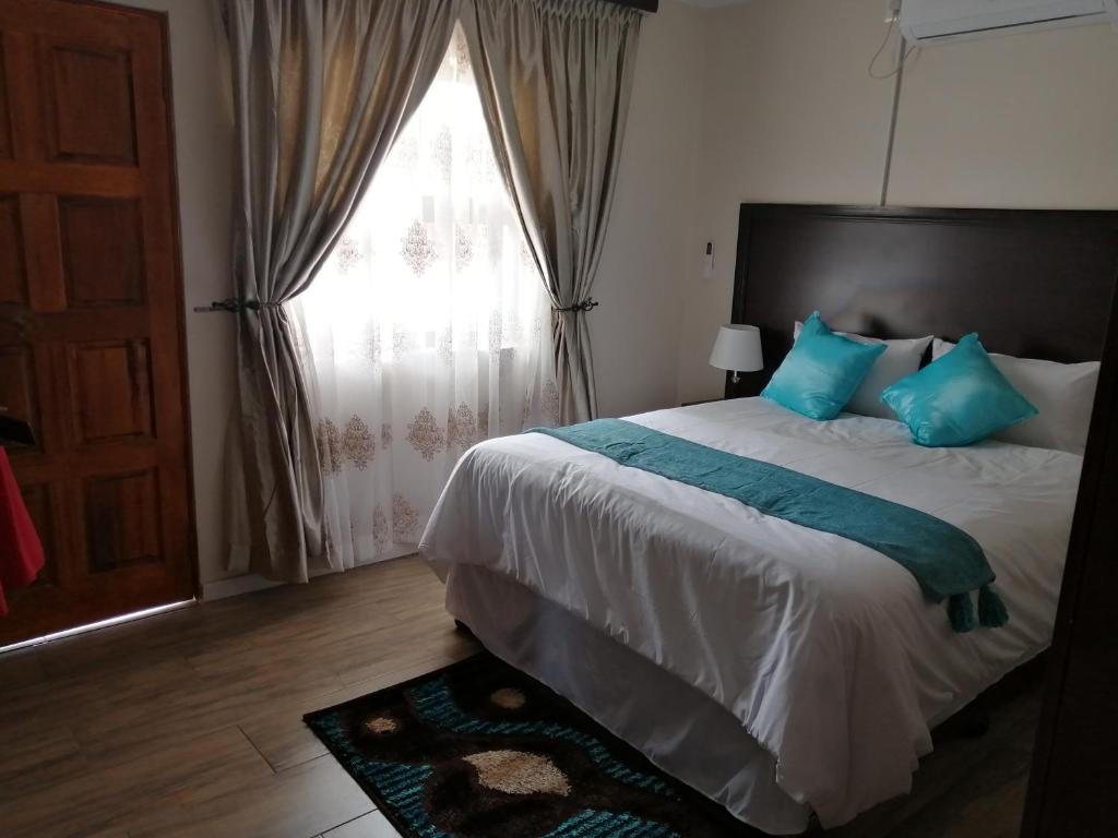 a bedroom with a bed with blue pillows and a window at LALA POA GUEST HOUSE in Klerksdorp