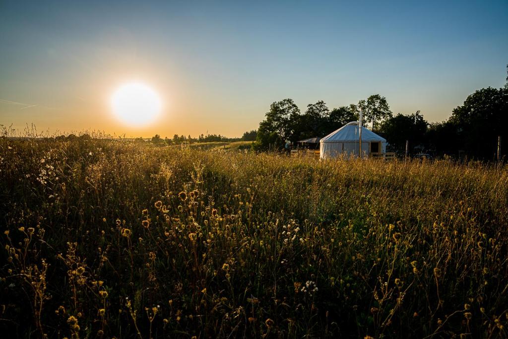 un granero en un campo con la puesta de sol en el fondo en Siedlisko pod Krukiem - Jurta en Suwałki