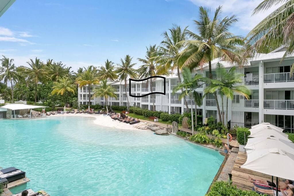 a swimming pool with palm trees and a building at Beach Club Port Douglas 3 Bedroom Penthouse in Port Douglas