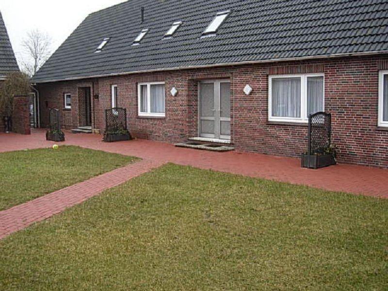 une maison en briques avec une pelouse devant elle dans l'établissement Nordsee-Ferienanlage-Wohnung-Baltrum, à Dornumersiel