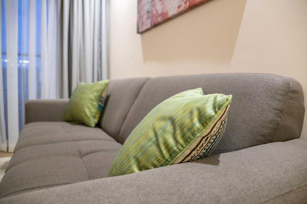 a gray couch with two green pillows on it at Kozi Suites Nairobi Airport in Nairobi