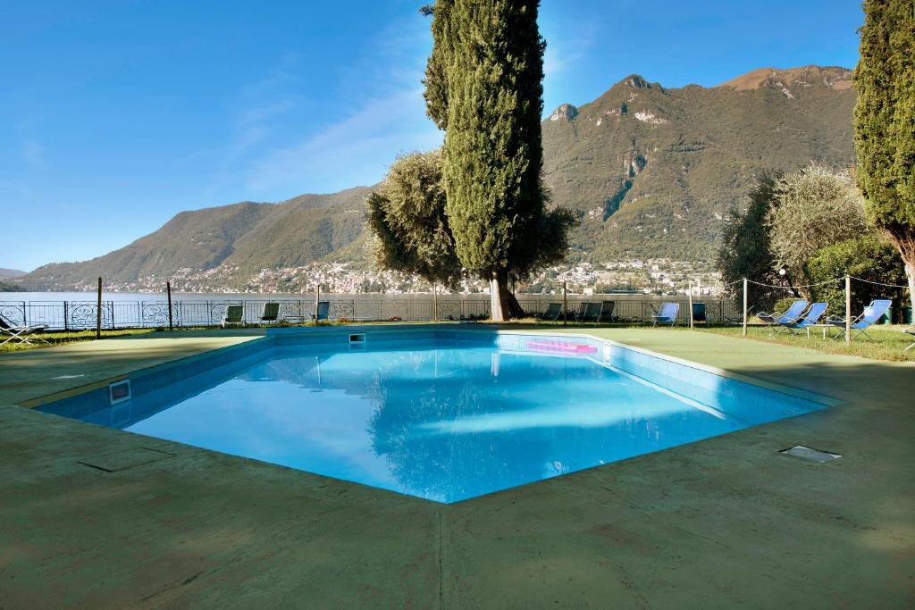a swimming pool with a tree and mountains in the background at Residence La Cava Trilocale 1d in Pognana Lario