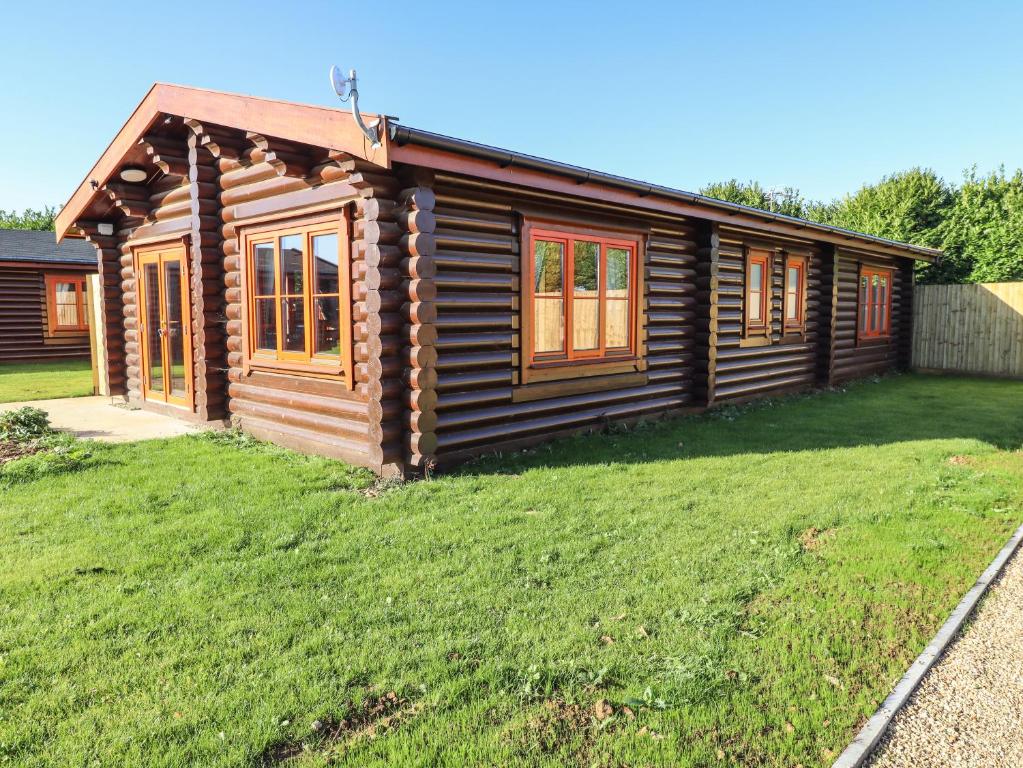 una cabaña de madera con un patio de césped delante de ella en Holly Lodge en Oakham