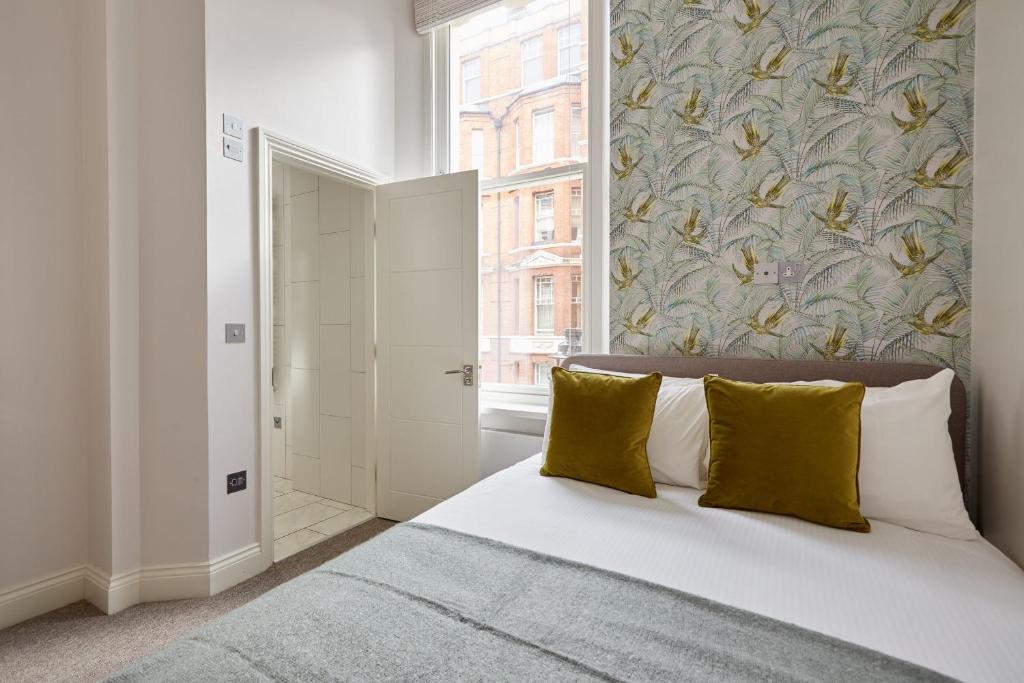 une chambre avec un lit avec des oreillers jaunes et une fenêtre dans l'établissement 2VH Virginia House, 31 Bloomsbury Way by City Living London, à Londres