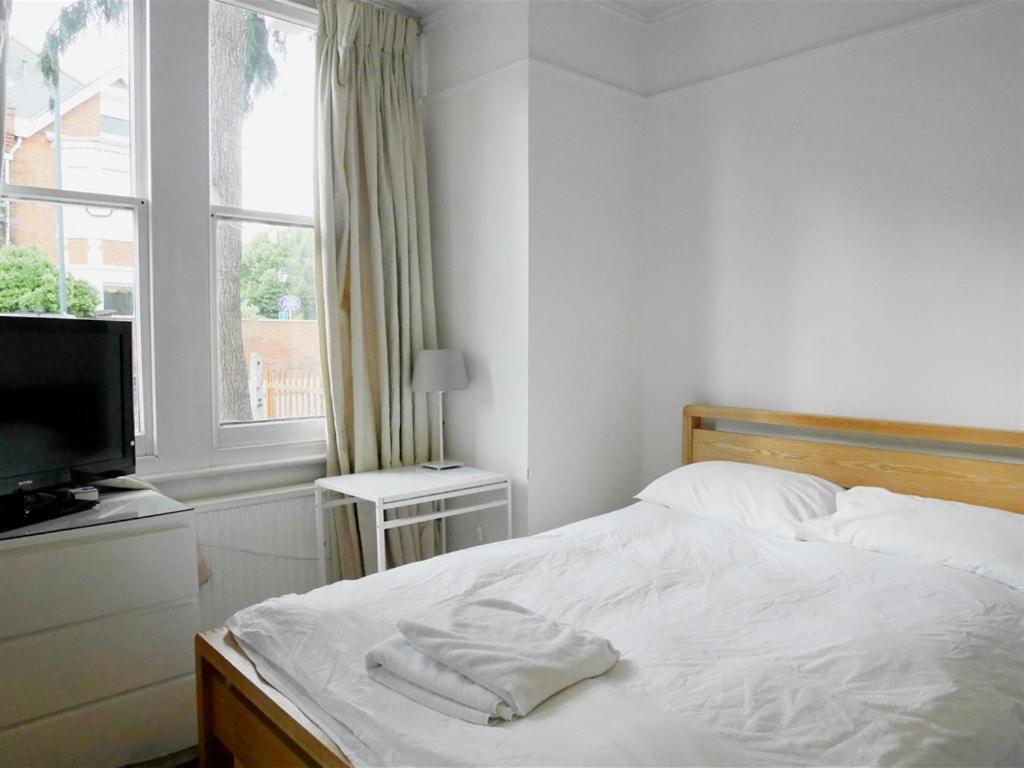 a white bedroom with a bed and a television at Kew Studios and Rooms in Kew