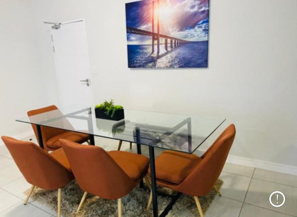 une table en verre avec des chaises orange dans la chambre dans l'établissement 3 Bedroom apartment at The Blyde, à Pretoria