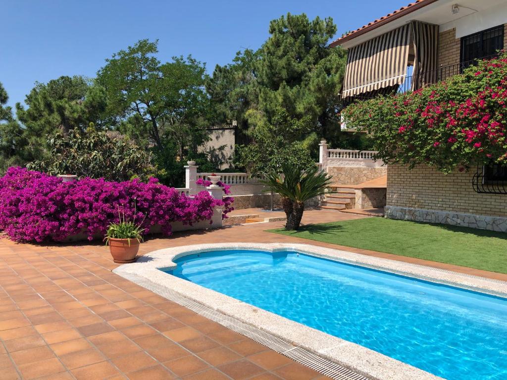a swimming pool in front of a house with purple flowers at Villa Dolcedo in Lloret de Mar