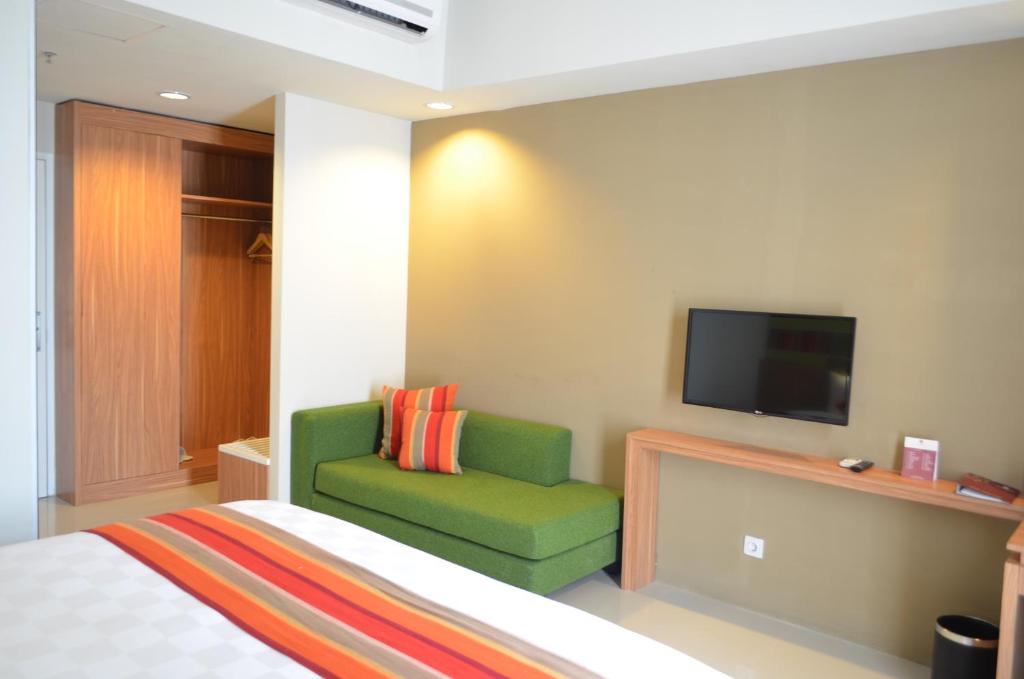 a bedroom with a bed and a green chair and a tv at Kyriad Hotel Airport Jakarta in Tangerang