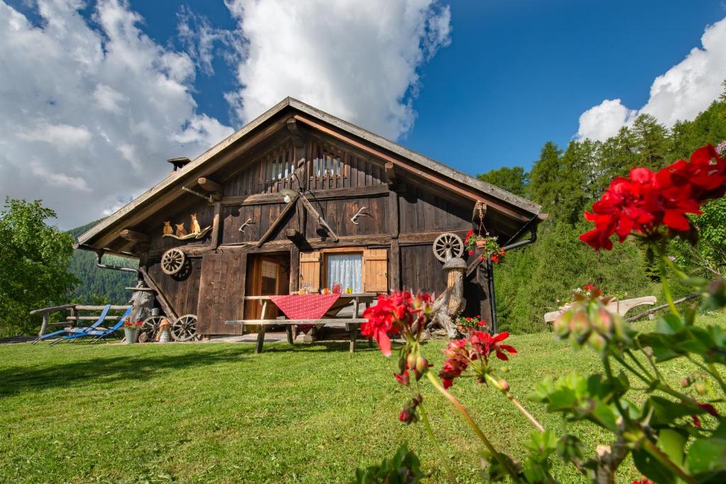 a log cabin with red flowers in front of it at Baita Mas Socina in Peio