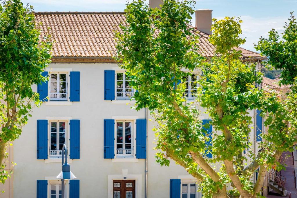 uma casa branca com persianas azuis e árvores em Maison d'hôtes ÔVillage em Ouveillan