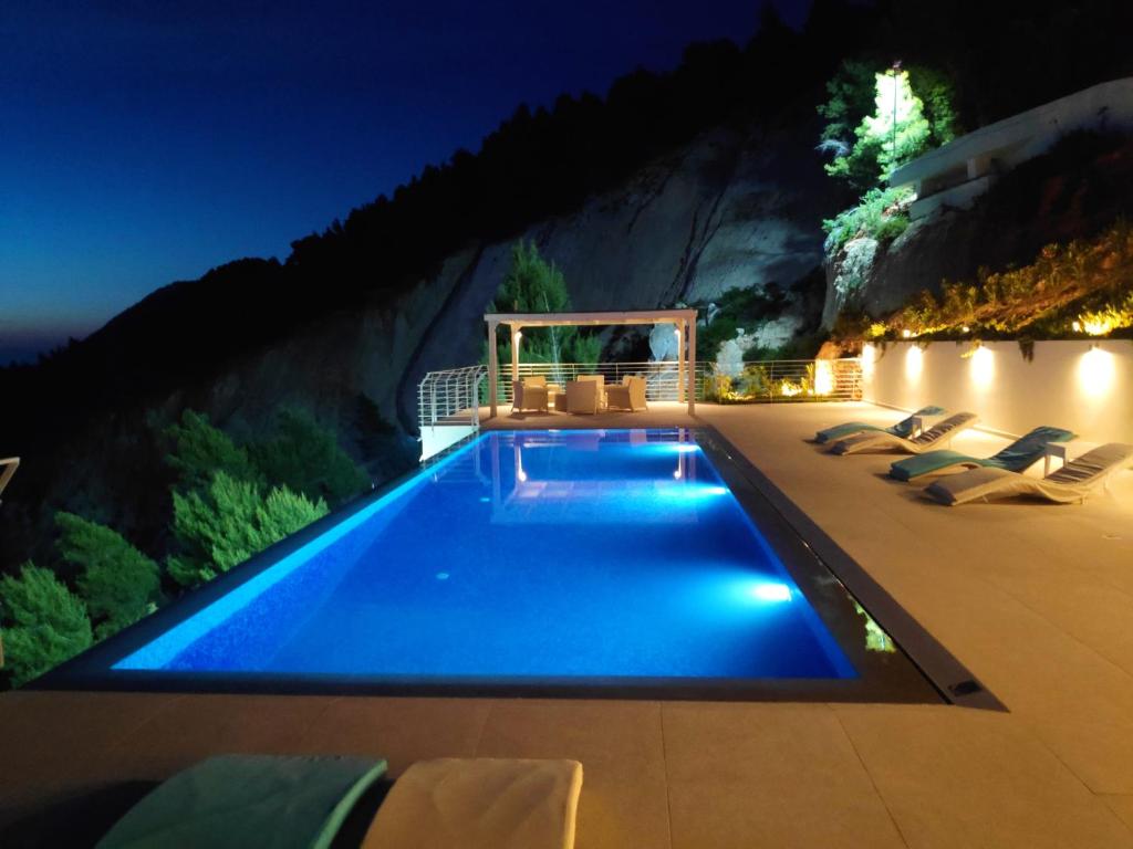 basen w nocy z krzesłami wokół niego w obiekcie Okeanos Luxury Villas - Resort w mieście Athanion