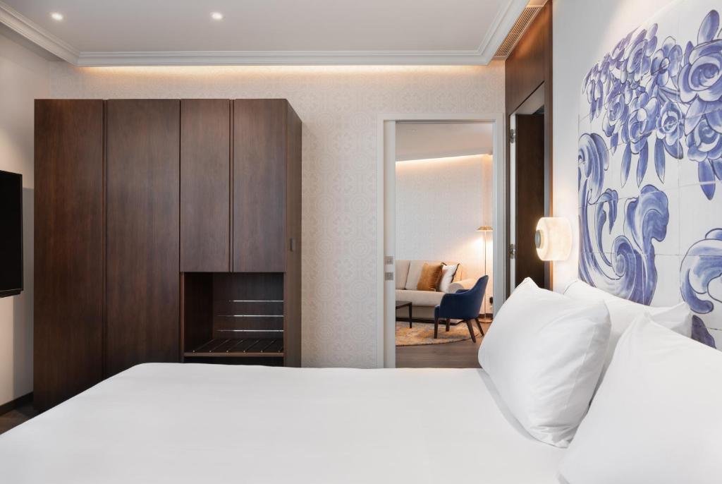 A bedroom with a large white bed, dark wardrobe and a glimpse into a separate sitting area.