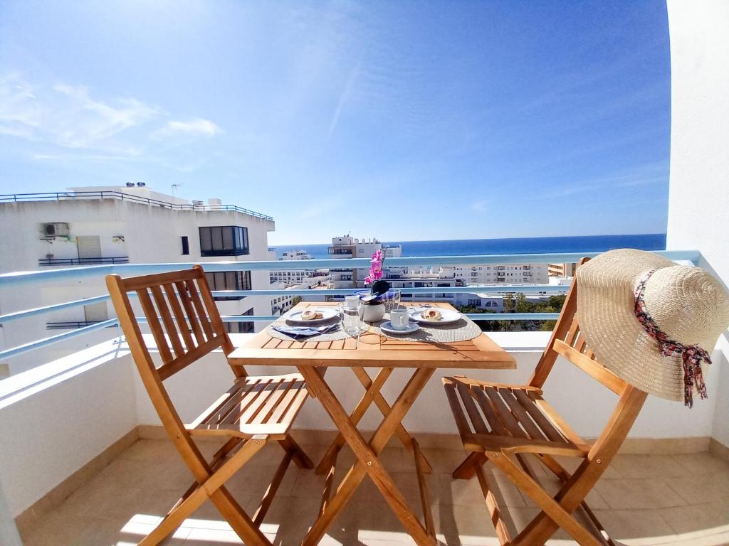 een tafel en 2 stoelen op een balkon met uitzicht op de oceaan bij COLINA FÉRIAS- Garagem & WIFI in Quarteira