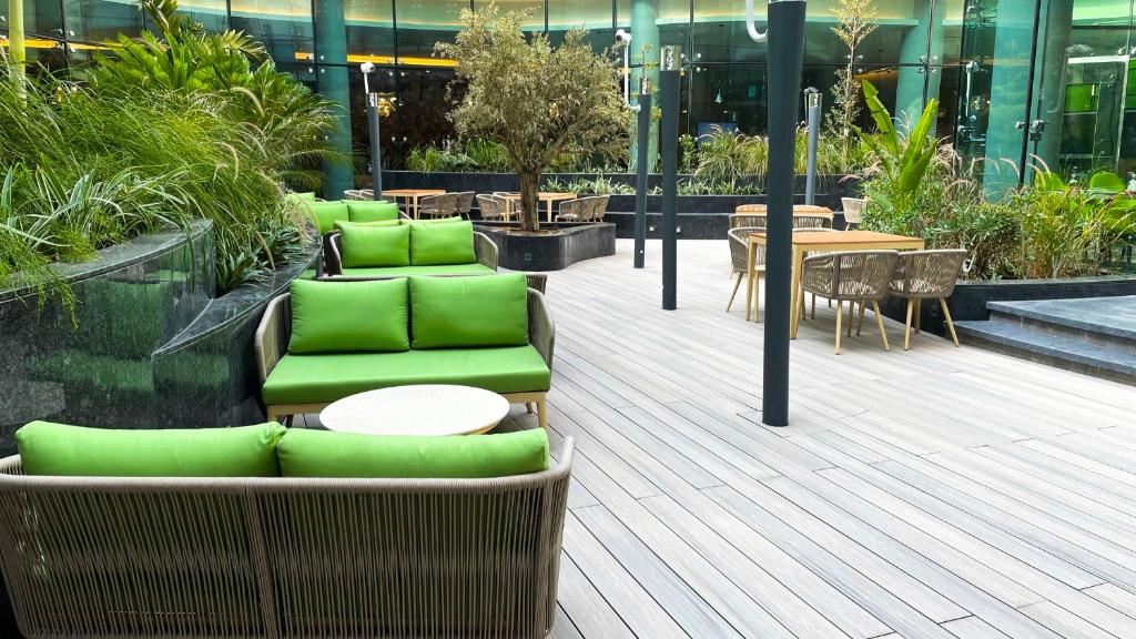 Al Khoory Sky Garden Hotel في دبي: فناء مع كراسي خضراء وطاولات في مبنى