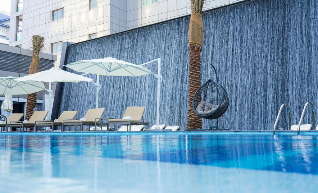a swimming pool with umbrellas and chairs and a fountain at Al Khoory Sky Garden Hotel in Dubai