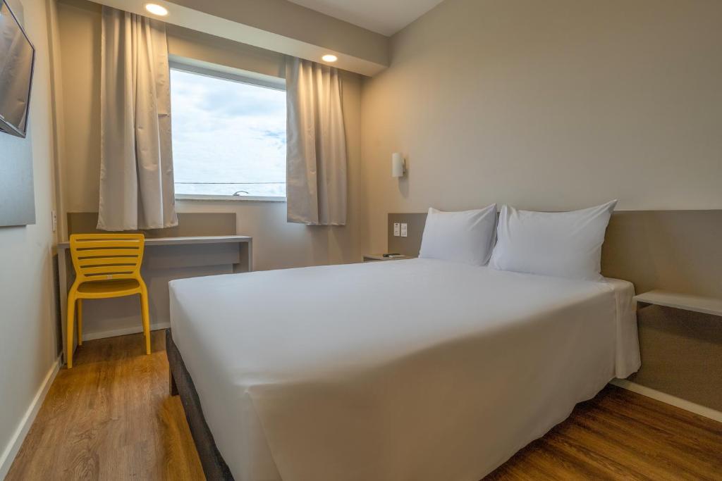a bedroom with a large white bed and a yellow chair at Transamerica FIT Primavera do Leste in Primavera do Leste