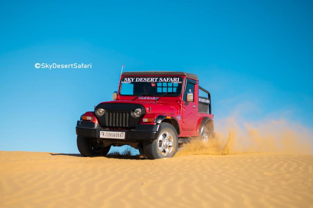 a red truck driving through the sand in the desert at Sky Desert Safari in Sām