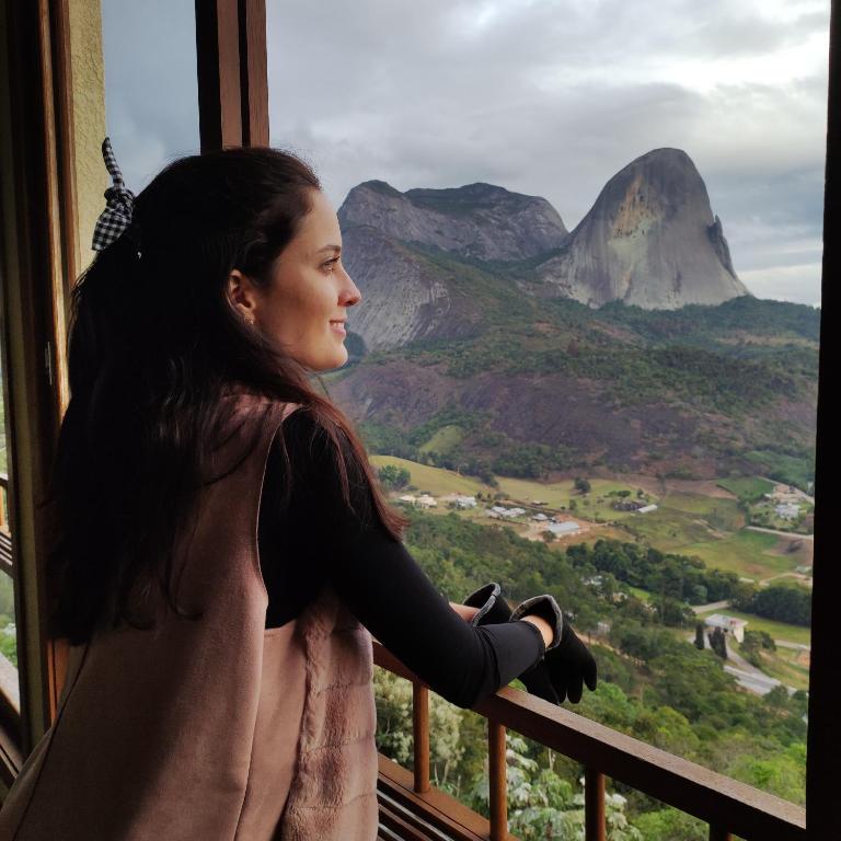 a woman standing in a window looking out at a mountain at Nosso Flat Pedra Azul - Condomínio Vista Azul in Domingos Martins