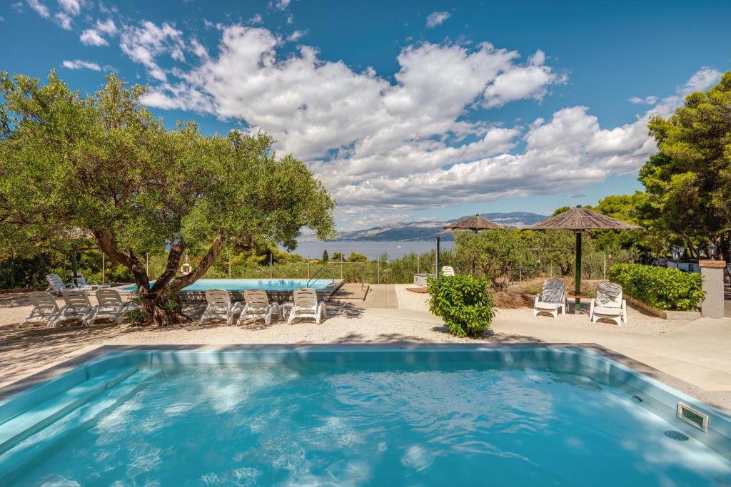 a swimming pool with chairs and a table and trees at Waterman Beach Village in Supetar