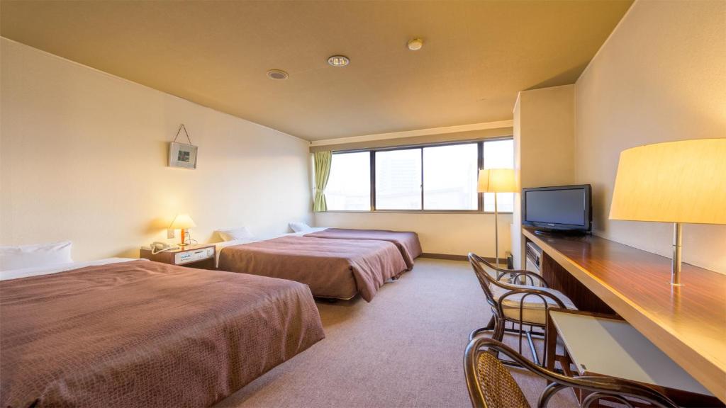 山形市にあるホテルさくらんぼのベッド2台、デスク、テレビが備わるホテルルームです。