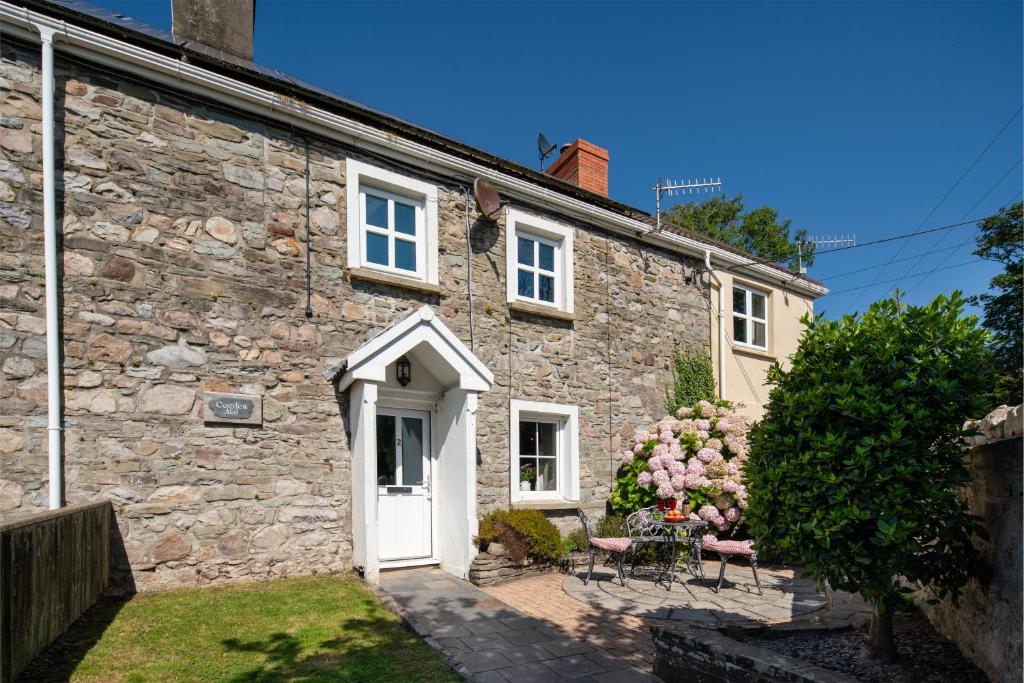 an old stone house with a white door and chairs at Coeden Afal in Kidwelly
