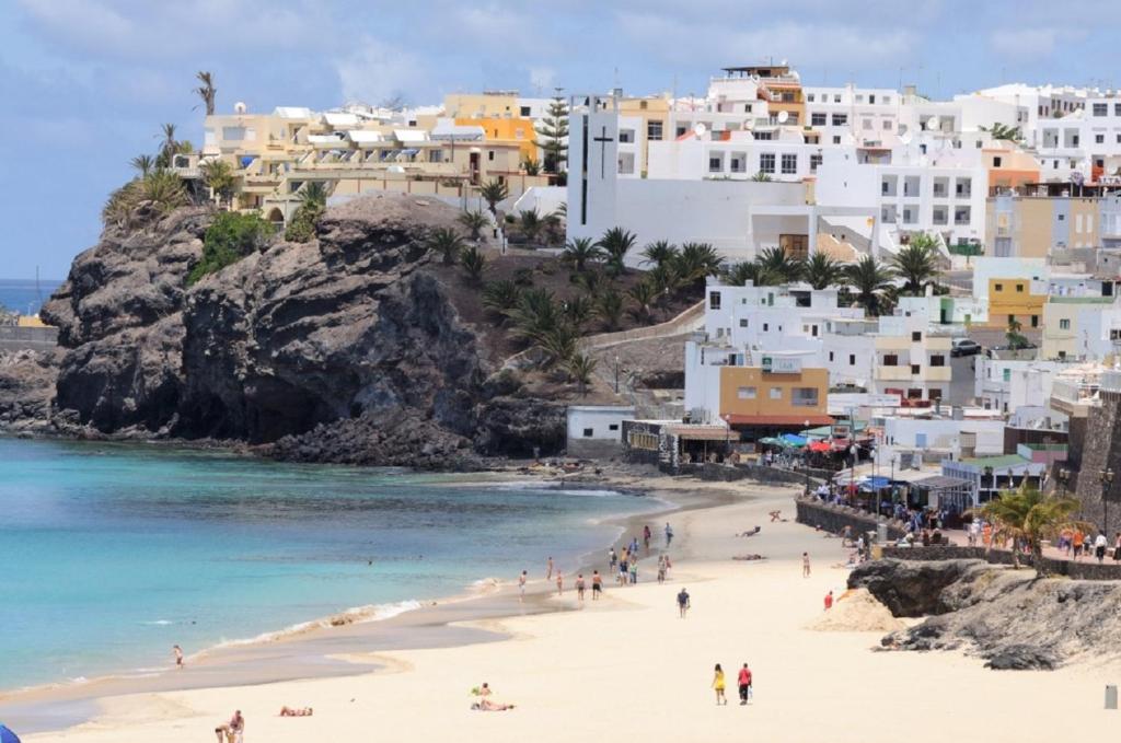 Grupa ludzi na plaży z budynkami w obiekcie Apartamentos El Carmen w mieście Morro del Jable