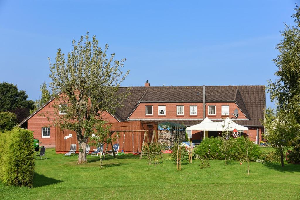a large red house with a garden in front of it at Ferienwohnung auf dem Ferienhof „Zur alten Linde“ in Holtgast