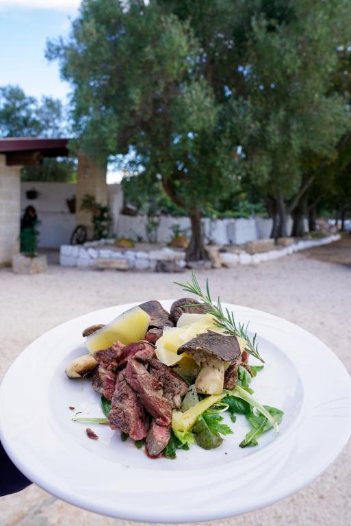 a white plate of food with meat and vegetables at Masseria Borgo Santuri in Ostuni