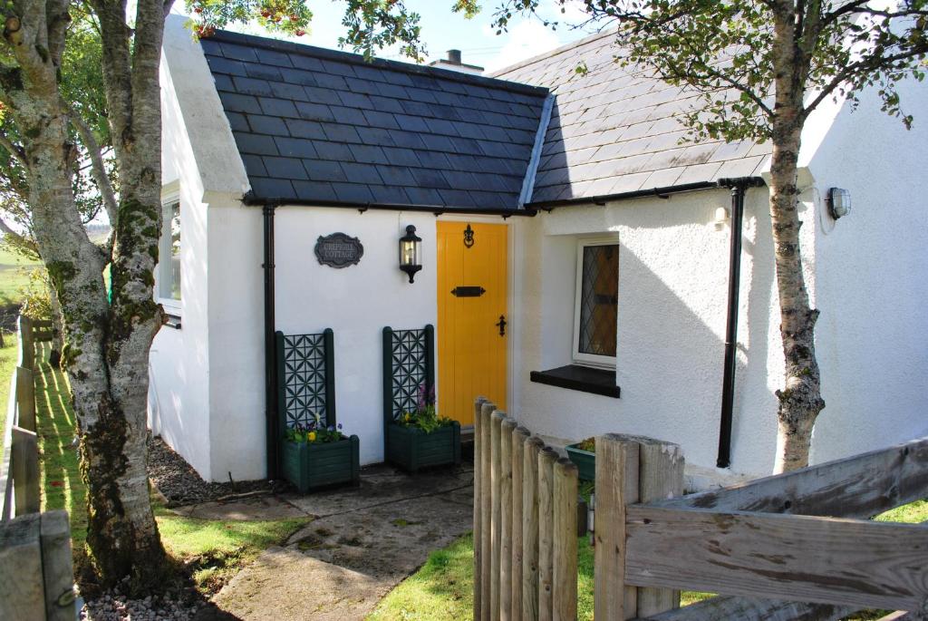 una pequeña casa blanca con puerta amarilla en Crepigill Cottage, en Portree