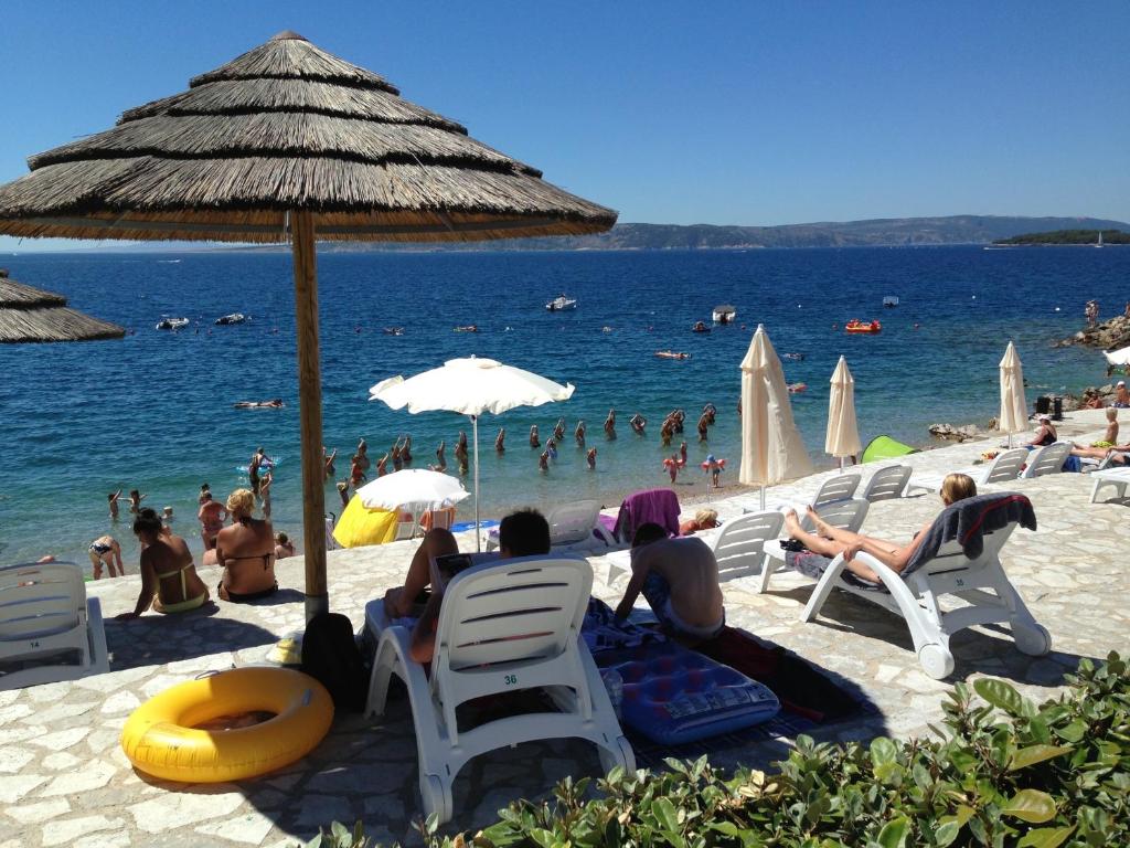 a group of people sitting on a beach with an umbrella at Easyatent Luxe Safari tent Krk in Krk