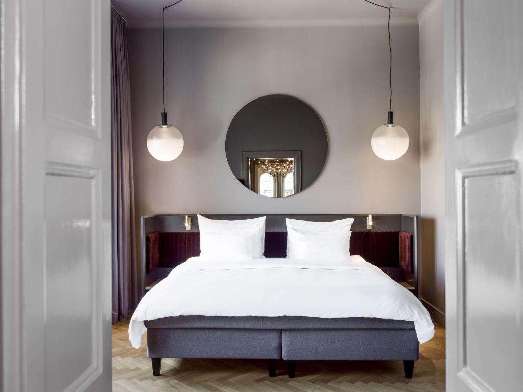 a bedroom with a bed with white sheets and a mirror at Radisson Collection, Strand Hotel, Stockholm in Stockholm