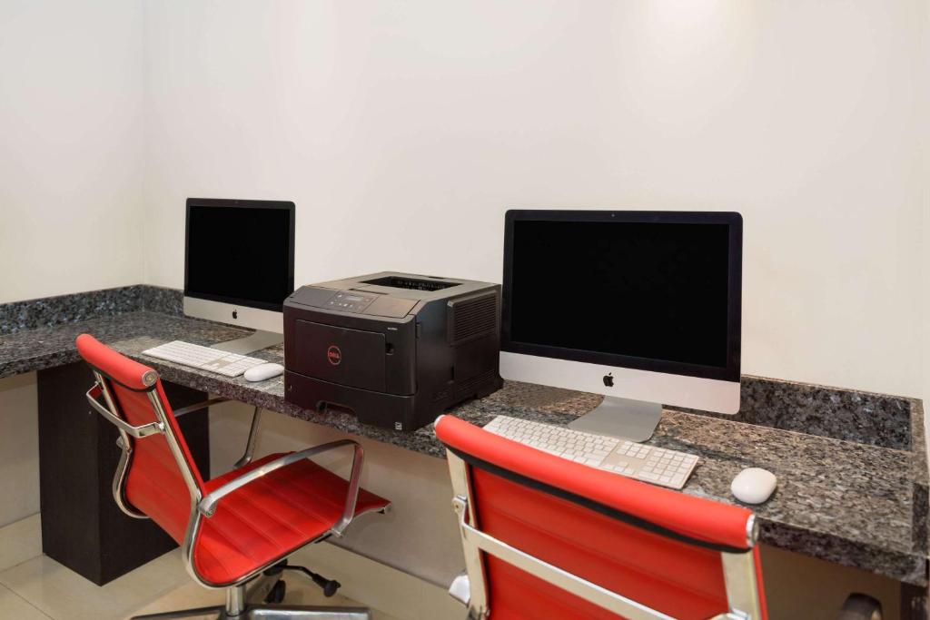 a desk with two computer monitors and a printer at Ramada by Wyndham Miami Springs/Miami International Airport in Miami