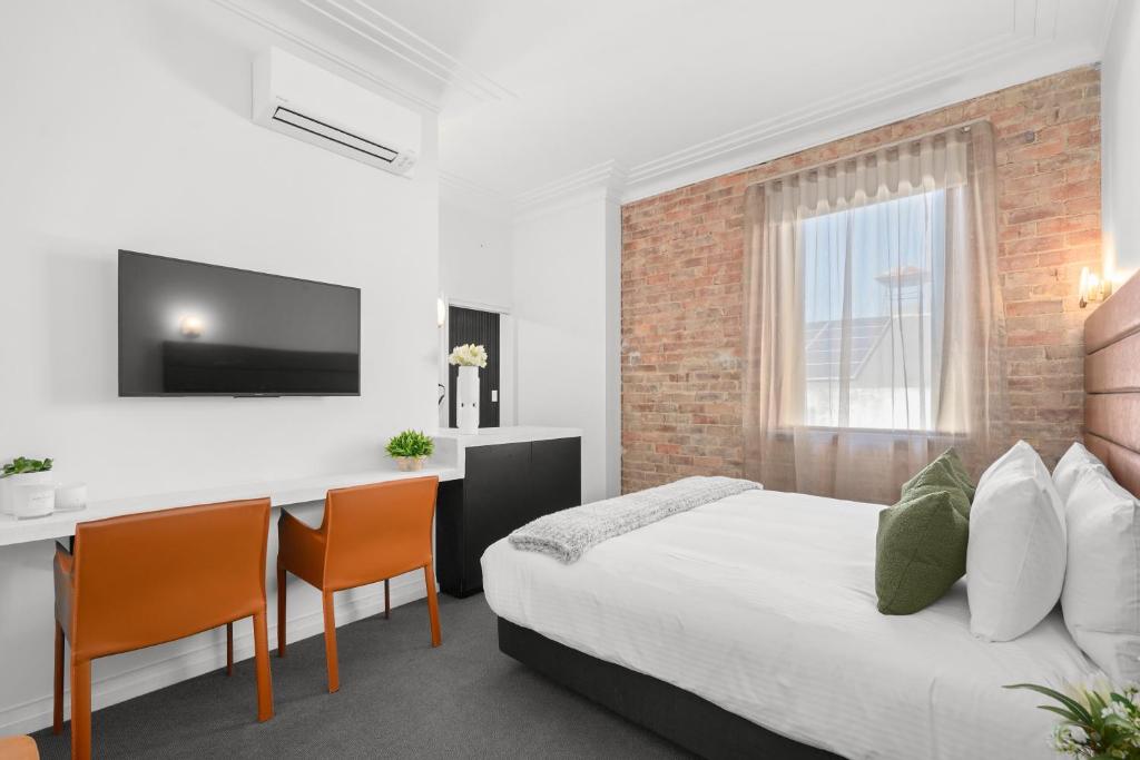 a room with a bed, chair, tv and a window at Grand Hotel and Studios in Wyong