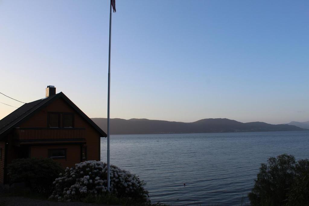 a house with a flag pole next to a body of water at Hjelvikhytta - flott beliggenhet ved sjøen in Hjelvik