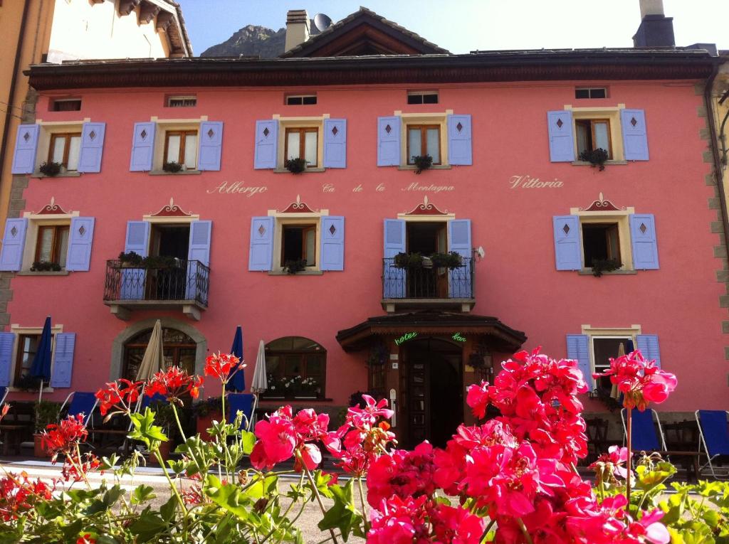 a pink building with flowers in front of it at Hotel Vittoria - Ca' De La Montagna in Montespluga