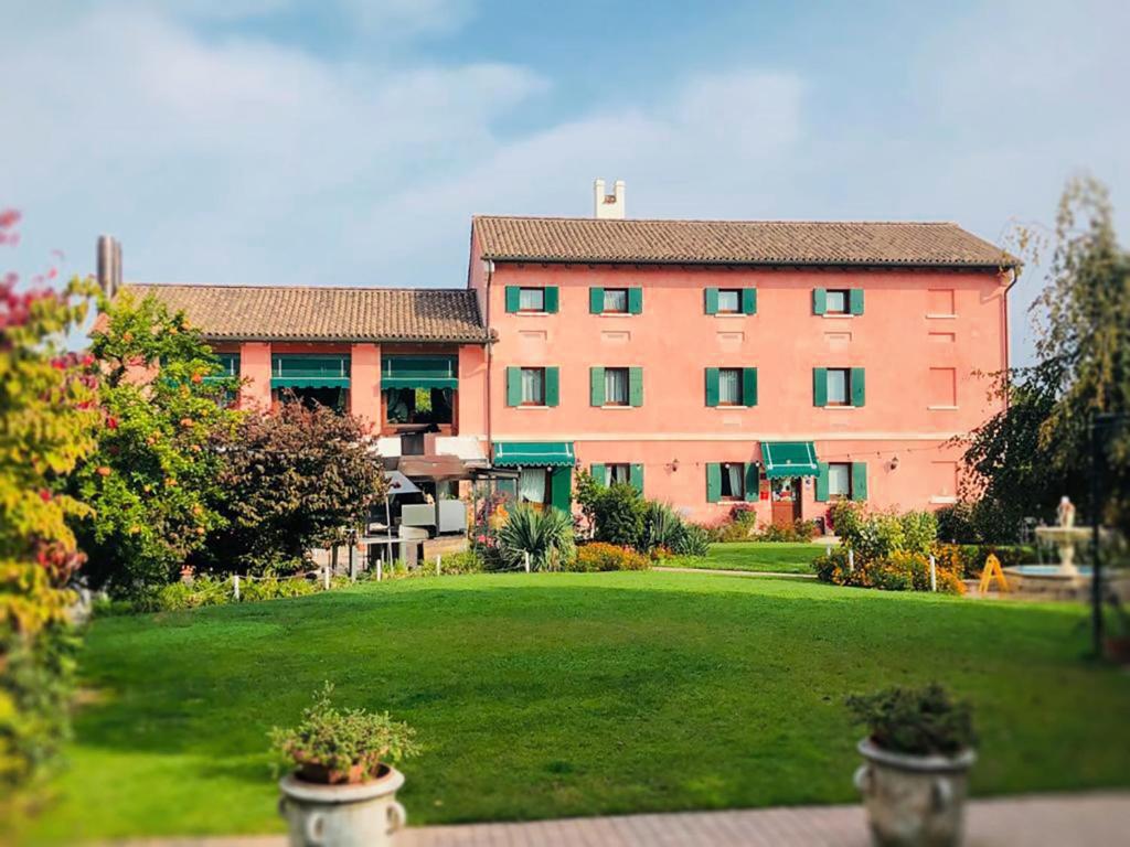 un grand bâtiment rose avec une pelouse verte devant lui dans l'établissement Osteria Alla Pasina, à Dosson