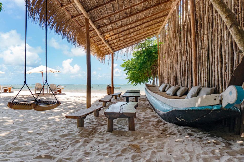 a boat on a beach with chairs and swings at Ventos Morere Hotel & Beach Club in Ilha de Boipeba
