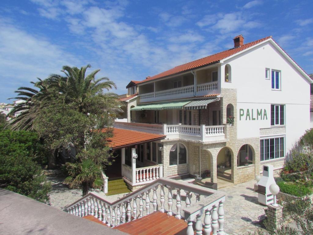 a large white house with a palm tree at Palma Guesthouse in Rab