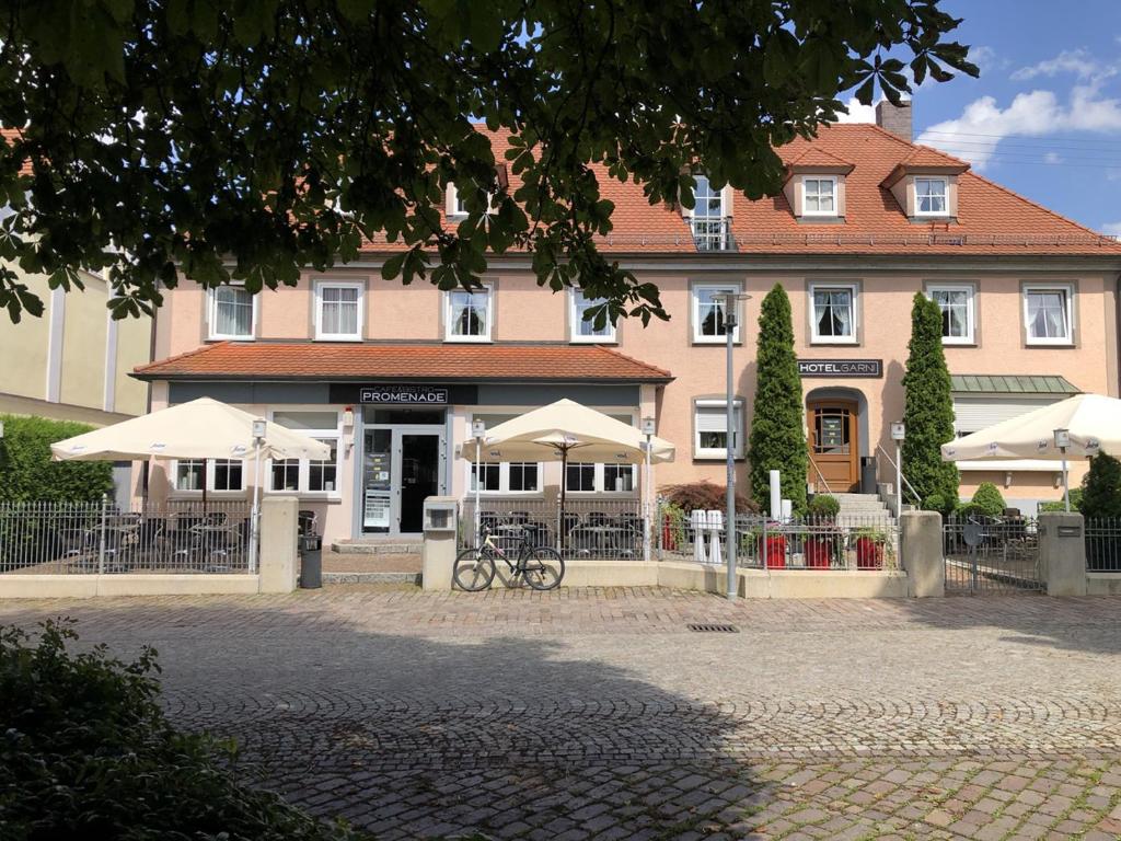 a large building with tables and umbrellas in front of it at Hotel Garni Promenade in Weißenhorn