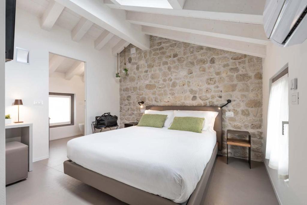 a bedroom with a white bed and a stone wall at Portone180 Guest House in Roveredo in Piano
