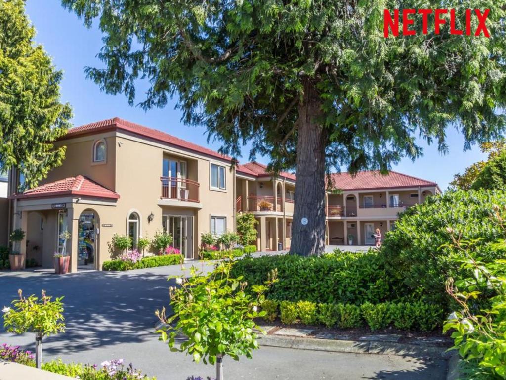 uma casa grande com uma árvore em frente em Roma On Riccarton Motel em Christchurch