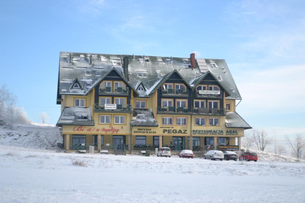 een groot geel gebouw met auto's geparkeerd in de sneeuw bij Ośrodek Pegaz in Duszniki Zdrój