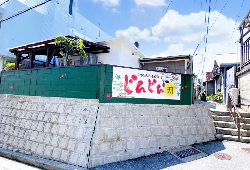 un cartel en una pared frente a un edificio en Okinawa Naha JinJin -沖縄伝統体験型宿じんじん- en Naha
