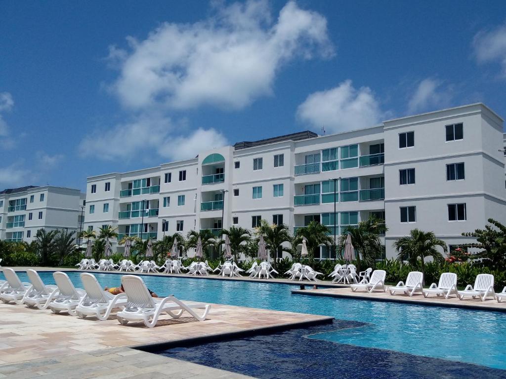 um hotel com uma piscina com cadeiras e um edifício em Palm Village Acqua - Apartamento Premium - Em frente à piscina - Porto de Galinhas em Porto de Galinhas