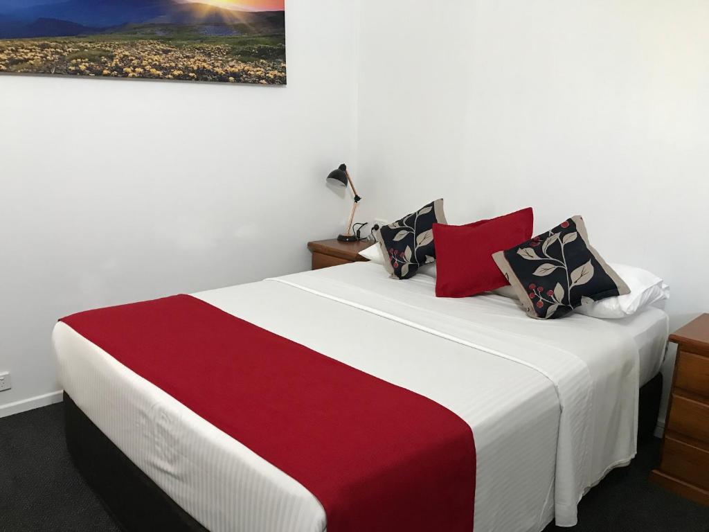 a bedroom with a large bed with red and white sheets at Royal Motel Tenterfield in Tenterfield